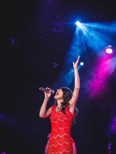 Woman with dark brown hair wearing a red dress and singing on a live show stage in Branson.