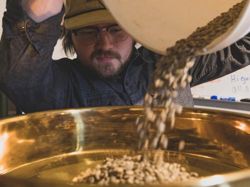 Man pouring coffee beans into a coffee roasting machine in Branson. 