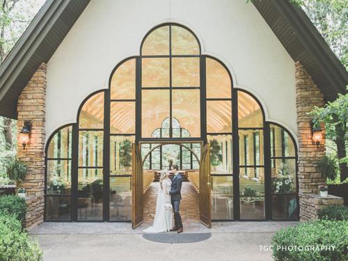 Recently married couple standing in front of a glass chapel in the Ozarks.