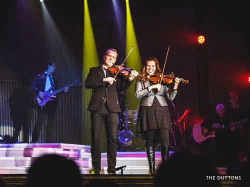 Brother and sister playing violins and singing on Branson stage.