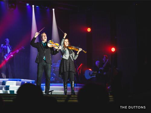 Brother and sister playing violins and singing on Branson stage.