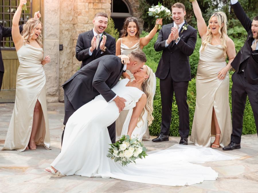 Pure celebration and romance! This unforgettable moment at Integrity Hills captures the groom dipping his bride for a kiss while the wedding party cheers them on—classic Branson wedding photography with heart and joy.