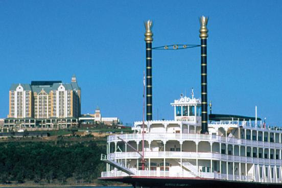 A paddleboat going down the river with a building in the background.
