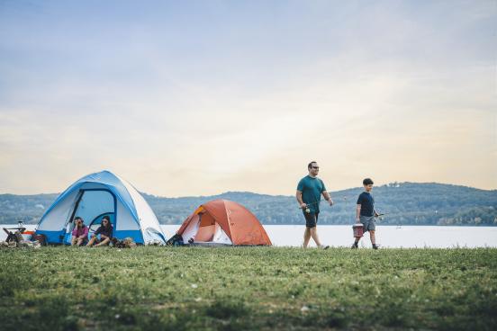 a mother and daughter relax in their tent while a father and son walk away with their fishing poles in hand
