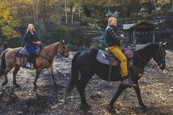 Husband and wife riding horses through a nature park in Branson in the fall.