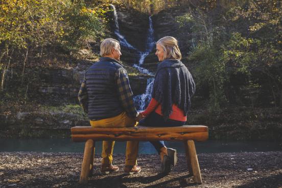 Man and woman sitting on a wooden bench surrounded by a scenic view of nature in Branson.