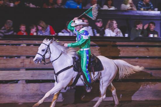 Man in green costume riding a horse and waving a flag. 