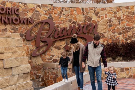 Husband and wife walking with young son and daughter in front of a sign in Downtown Branson.