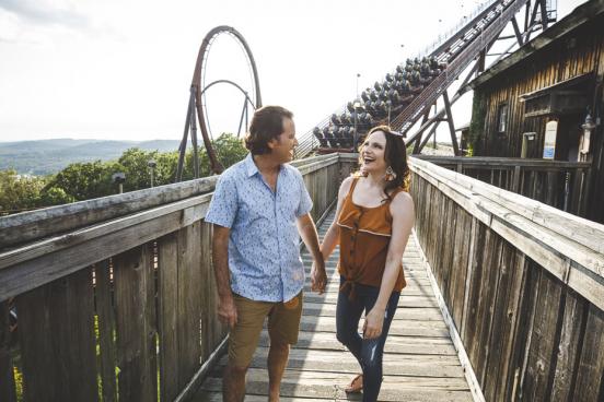 Couple holding hands and walking in front of a roller coaster ride at Silver Dollar City theme park in Branson.
