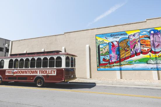 Free Downtown trolley driving in front of a Branson mural. 