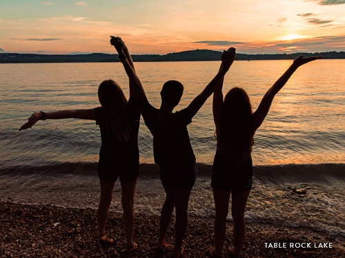 Three girls holding hands and staring into the sunset at Table Rock Lake.