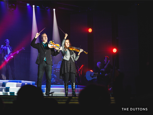 Brother and sister playing violins and singing on Branson stage.