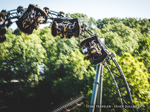 Three cars of a spinning roller coaster surrounded by green trees in Branson.