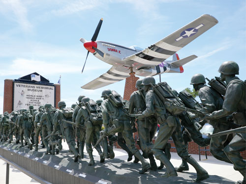 Statue of soldiers running and a plane flying in front of the Veterans Memorial Museum